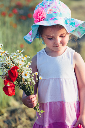 Lovely little girl in the field of wild flowers. Cute girl picking the spring flowers for her mom for Mother's Day in the meadow. Girl holding bouquet of flowers. Spending time close to natureの写真素材