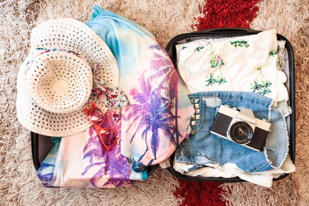 Time for summer vacation. Suitcase with packed summer clothes, a camera, a hat and sunglassesの写真素材