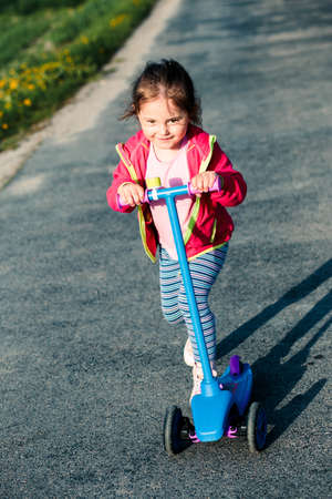 Little adorable girl having fun riding on scooter, playing outdoorsの写真素材