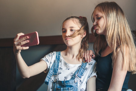 Young women taking selfie, using smartphone camera. Girls making faces, enjoying taking funny...