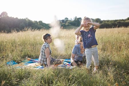Little girl making a hand gesture for taking picture. Family spending time together on a meadow, close to nature. Parents and kids sitting on a blanket on grass. Candid people, real moments, authentic situationsの写真素材