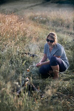 Woman roasting a marshmallow over a campfire on meadow. Vacations close to nature. Candid people, real moments, authentic situationsの写真素材