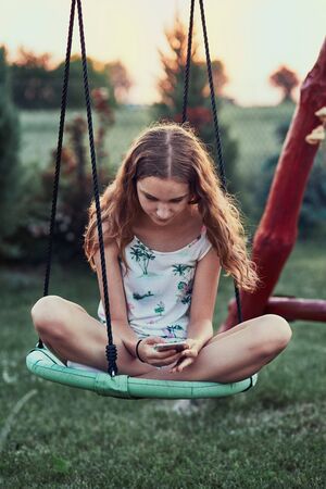 Young woman using mobile phone smartphone sitting on swing in a backyardの写真素材