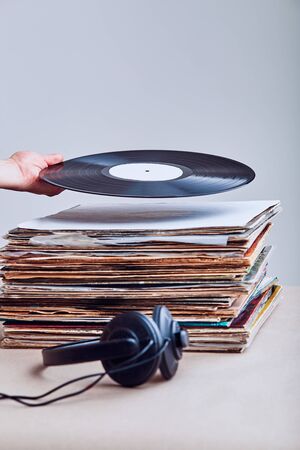 Woman taking vinyl from stack of many black vinyl records, headphones put at the front of vinyls. Copy space for text. Candid people, real moments, authentic situationsの写真素材