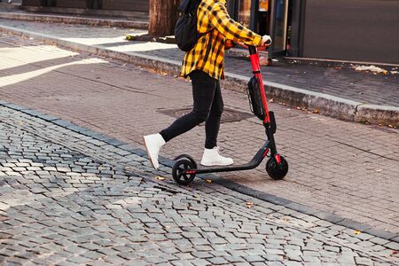 Girl using electric scooter in the street in downtown rented by using service on smartphone. Candid people, real moments, authentic situationsの写真素材