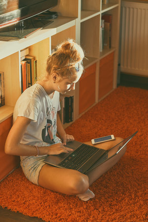 Young woman using portable computer and mobile phone, sitting on a floor, learning online at home....