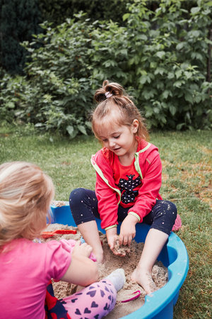 Children, little girls, playing in sandbox in playground outside on summer day. Real people,...