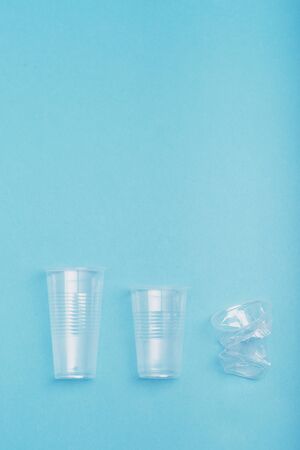 Squashed empty plastic cups put in a row, over blue background. Collecting plastic waste to recycling. Concept of plastic pollution and too many plastic waste. Copy space for textの写真素材