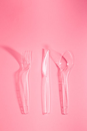 Plastic forks and knives scattered over pink background. Collecting plastic waste to recycling....