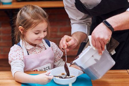 Chef adding hot melted chocolate with cocoa to container. Kid taking part in baking workshop. Baking classes for children,  aspiring little chefs. Learning to cook. Combining and stirring prepared ingredients. Real people, authentic situationsの写真素材