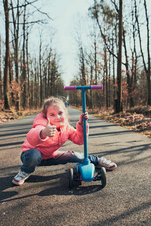 Little girl playing in the park, riding a scooter, having fun on sunny autumn day. Real people, authentic situationsの写真素材