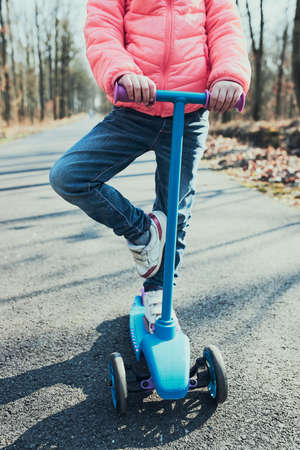 Little girl playing in the park, riding a scooter, having fun on sunny autumn day. Real people, authentic situationsの写真素材