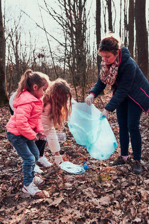 Family cleaning up a forest. Volunteers picking plastic waste to bags. Concept of plastic pollution and too many plastic waste. Environmental issue. Environmental damage. Responsibilitiy for environment. Real people, authentic situationsの写真素材