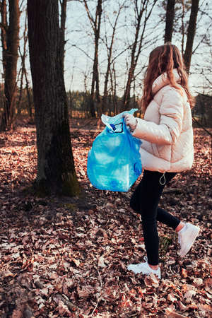Young woman cleaning up a forest. Volunteer picking plastic waste to bags. Concept of plastic pollution and too many plastic waste. Environmental issue. Environmental damage. Responsibilitiy for environment. Real people, authentic situationsの写真素材