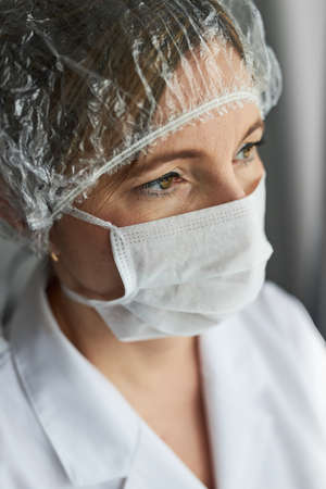 Doctor with face covered with mask. Portrait of young woman wearing the uniform, cap and mask to avoid virus infection and to prevent the spread of disease. Real people, authentic situationsの写真素材