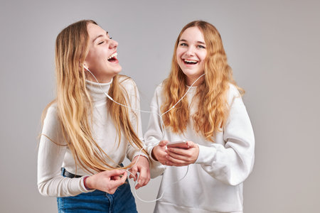 Young women girls listening to music together streaming content having fun watching video enjoying...