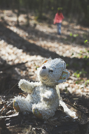 Little girl child walking away left forgot teddy bear on stump in a forest during a trip