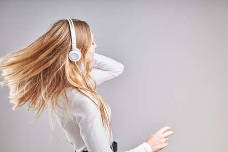 Young woman girl listening to music streaming content having fun watching video enjoying video chat talking with friends making gestures faces using smartphone earphones headphones standing over plain grey backgroundの写真素材
