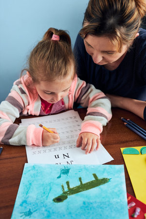 Little girl preschooler learning to write letters with help of her mother. Kid writing letters,...