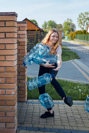 Young woman throwing out empty used plastic water bottles into trash bin. Collecting plastic waste...
