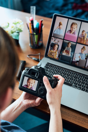 Female photographer working on photos on laptop and camera. Woman editing retouching browsing photos working as a freelancer sitting at deskの写真素材