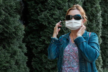 Woman walking outdoors wearing face mask during pandemic coronavirus outbreak standing at front of...