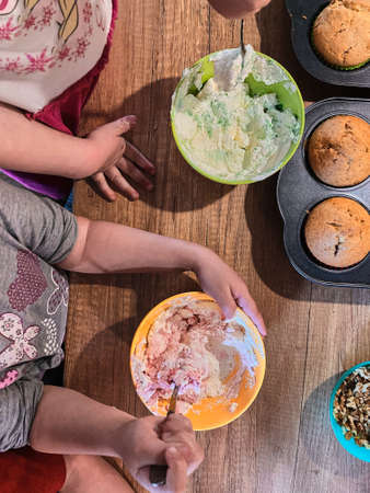 Group of children baking cupcakes, preparing ingredients, toppings, sprinkles for decorating cookies. Kids learning to cook, working together in kitchen at home. Concept of happy familyの写真素材