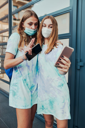 Young women girls taking selfie photos using smartphone standing at store front downtown. Girls...