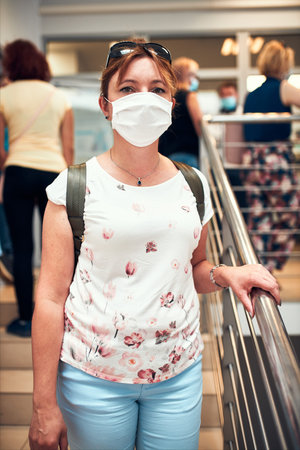 Woman going downstairs in public place inside wearing face mask to cover mouth and nose during...