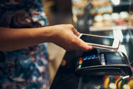 Woman paying in coffee shop using contactless method of payment via mobile phone.の写真素材