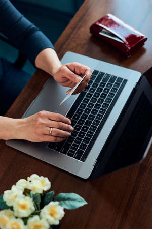 Female hands holding credit card over a keyboard of laptop sitting at a desk buying goods online from homeの写真素材