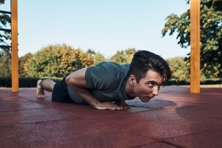 Young man doing push-ups on a red rubber ground during his workout in a modern calisthenics street...