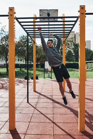 Young man bodybuilder exercising on monkey bars during his workout in a modern calisthenics street...
