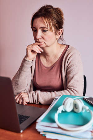 Woman focused on her work working hard doing her job remotely on laptop from home. Woman sitting at desk in front of computer looking at screen. Concept of remote workingの写真素材
