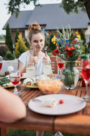 Young woman having a meal from grill during summer family picnic outdoor dinner in a home garden....