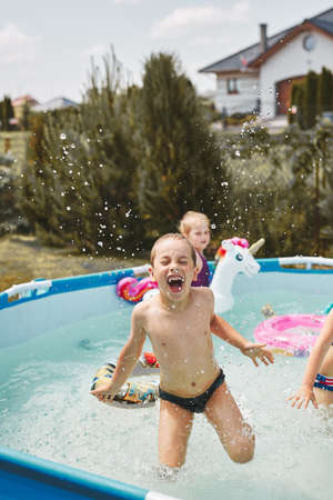 Boy jumping in a pool enjoying splashing having fun with siblings on a summer sunny dayの写真素材