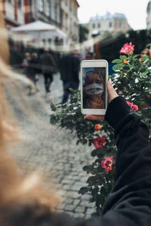 Young woman having video call talking while walking downtown in the evening wearing the face mask to avoid virus infection and to prevent the spread of disease in time of coronavirusの写真素材