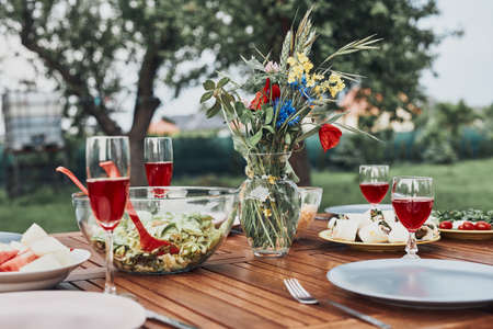 Dinner in an apple orchard garden on wooden table with salads and wine decorated with flowers. Close up of table with food prepared for family dinnerの写真素材