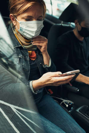 Woman talking on phone using smartphone sitting in a car wearing the face mask to avoid virus infection and to prevent the spread of disease in time of coronavirusの写真素材
