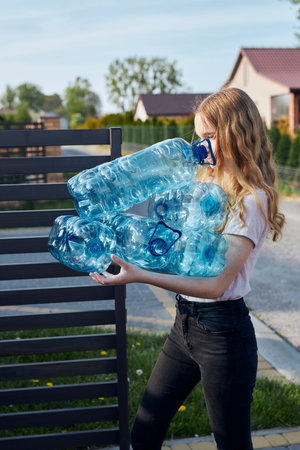 Young woman throwing out empty used plastic water bottles into trash bin. Collecting plastic waste...
