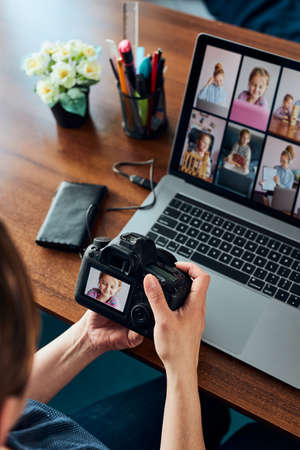 Female photographer working on photos on laptop and camera. Woman editing retouching browsing photos working as a freelancer sitting at deskの写真素材