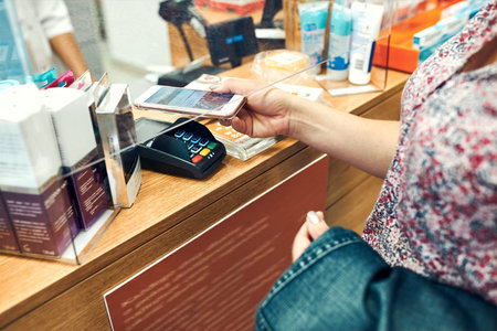 Woman paying for medicines at pharmacy using contactless method of payment via mobile phone. Woman...