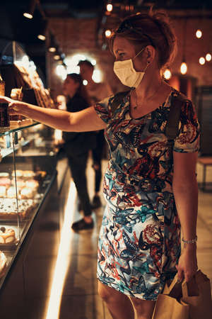 Young woman shopping in grocery store in the evening, wearing the face mask to avoid virus infection and to prevent the spread of disease in time of coronavirusの写真素材