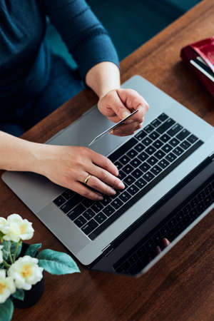 Woman doing online shopping using debit card and laptop. Female hands holding credit card over a keyboard of laptop sitting at a desk buying goods online from homeの写真素材