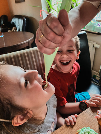 Child eating whipped cream squeezed stright from confectionery bag, during preparing toppings, baking cupcakes, decorating cookies. Kids cooking, working together in kitchen at home. Concept of happy familyの写真素材