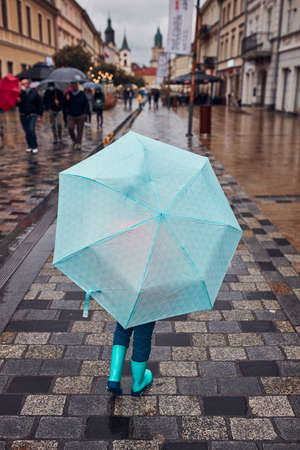 Back view of child holding big blue umbrella walking in a downtown on rainy gloomy autumn dayの写真素材