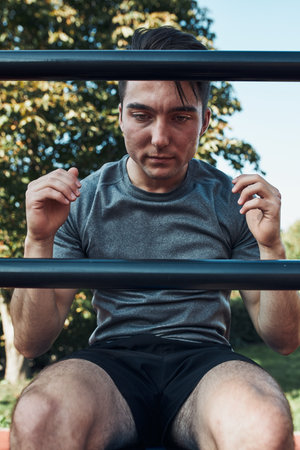 Young man doing sit-ups during his workout in a modern calisthenics street workout park. Man sitting...
