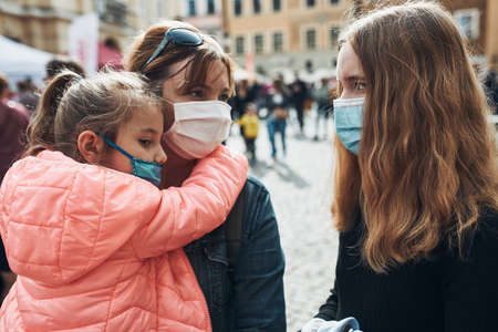 Family mother and her daughters standing in a street downtown wearing the face masks to avoid virus infection and to prevent the spread of disease in time of coronavirusの写真素材