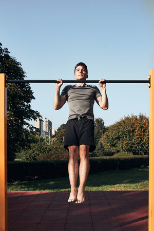 Young man doing pull-ups on pull-up horizontal bar during his workout in a modern calisthenics...