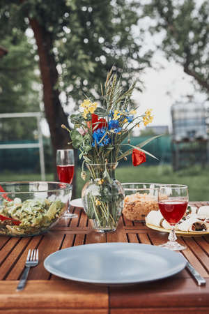 Dinner in an apple orchard garden on wooden table with salads and wine decorated with flowers. Close up of table with food prepared for family dinnerの写真素材